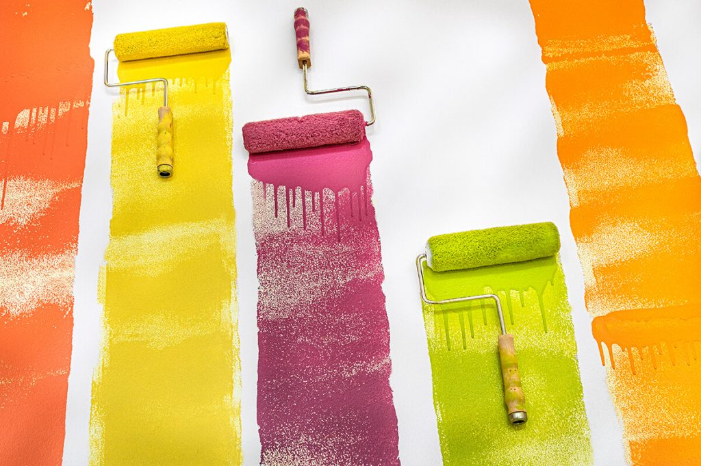Paint rollers on a white surface with colorful paint lines coming from them