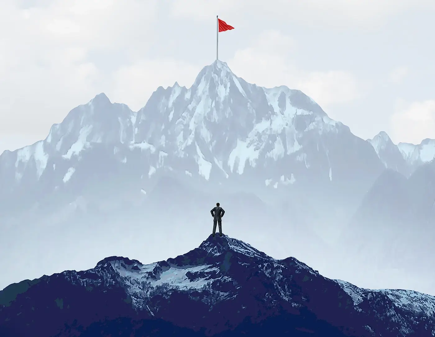 A man directly underneath the shadow of a large mountain with a red flag on top